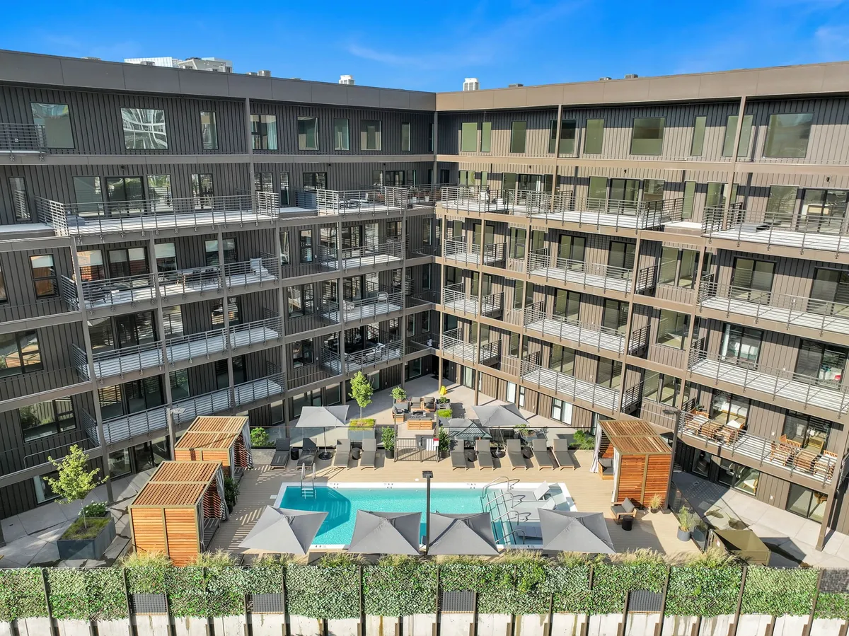 An inviting outdoor swimming pool surrounded by modern lounge chairs and lush landscaping, with balconies overlooking the pool area. The scene captures guests swimming, sunbathing, and socializing in a relaxed, resort-like environment, with the possibility of sunset views from the balconies.