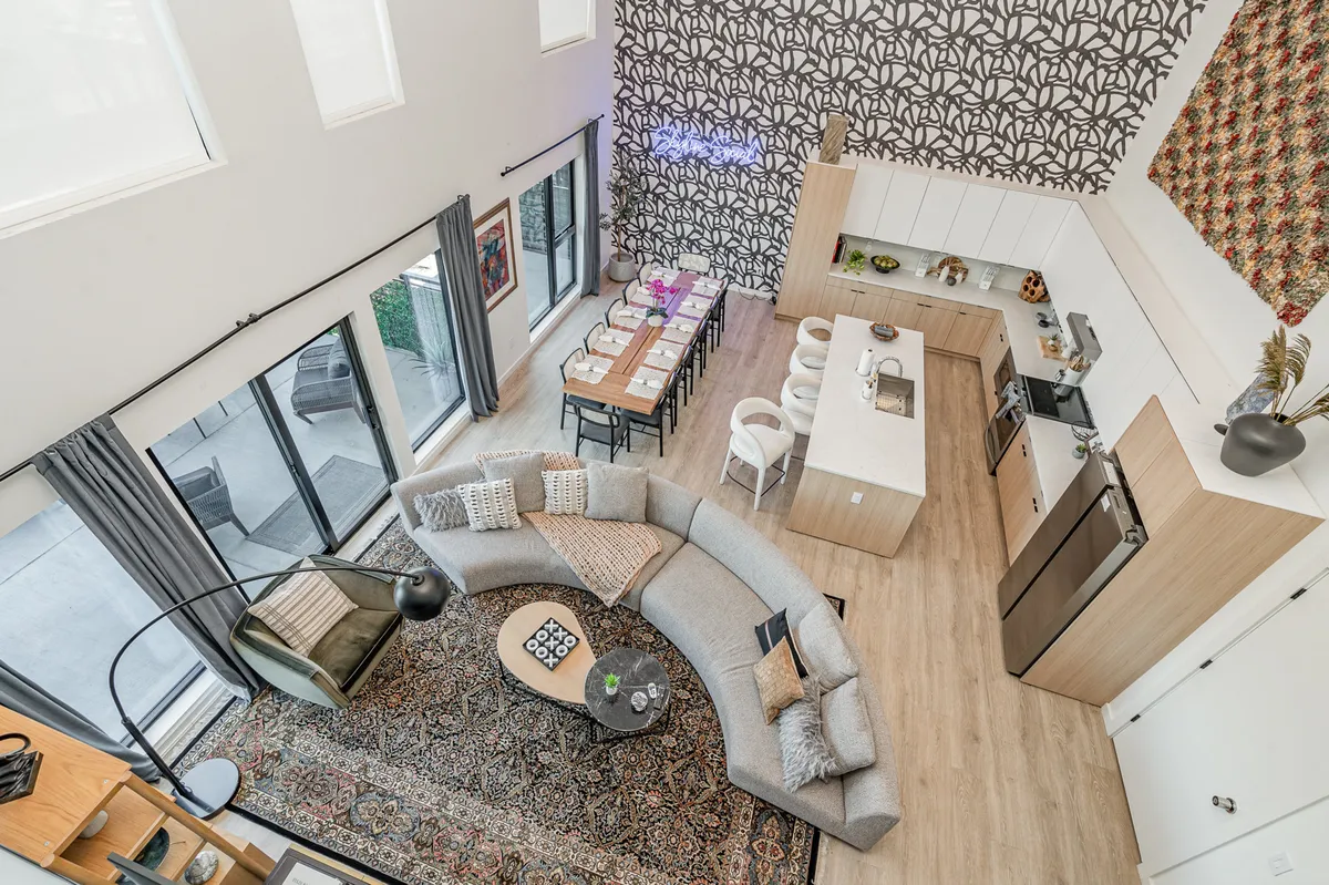 A spacious, sunlit open-concept living area featuring a modern curved sectional sofa arranged for socializing, a large dining table ready for celebratory meals, a sleek kitchen island perfect for gathering, and a stylish decorative accent wall that adds a touch of contemporary flair.