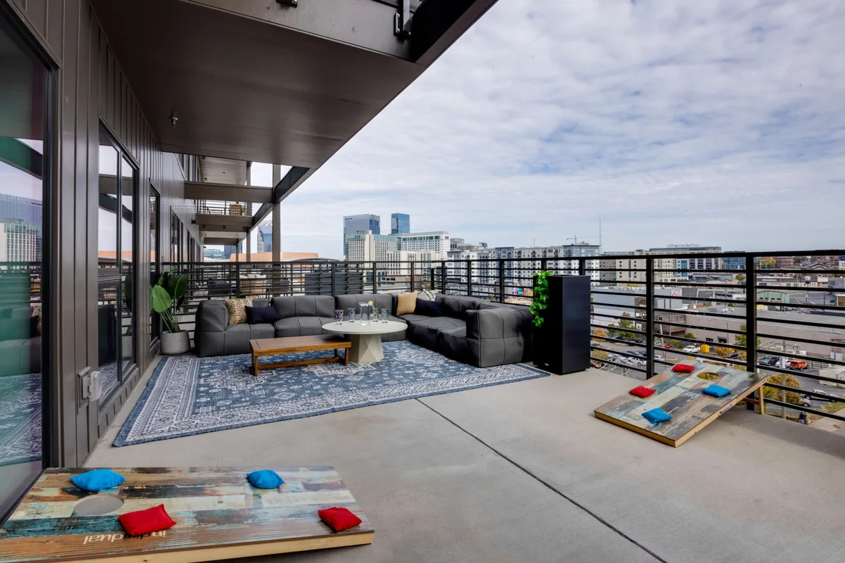 A spacious outdoor seating area features comfortable lounge furniture arranged atop a decorative rug, with a sweeping view of the Nashville city skyline serving as the backdrop. The setup invites gatherings, relaxation, and social activities, and the space is designed for both entertaining and unwinding. Evidence of outdoor games is visible, supporting playful group activities.