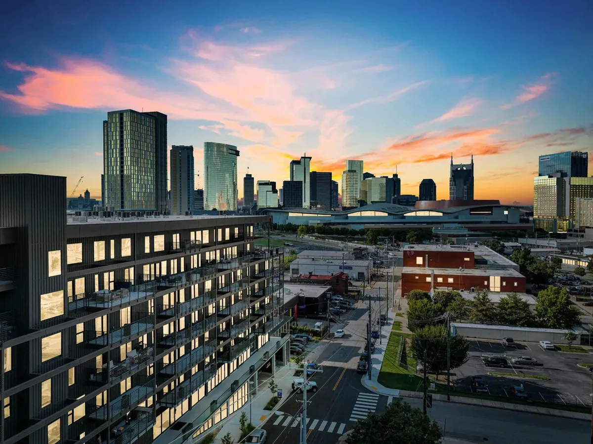 A panoramic view of the modern apartment building set against the city skyline at sunset. The image captures the excitement of urban exploration, with roadways leading into the heart of Nashville.