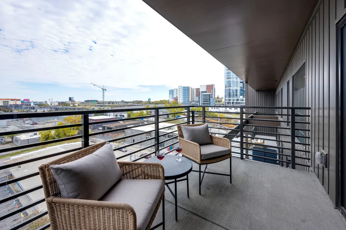 A private balcony features cozy seating and a small table set against an expansive city view. The calm, inviting mood makes it an ideal retreat for a morning coffee or an evening glass of wine while admiring the city from above.
